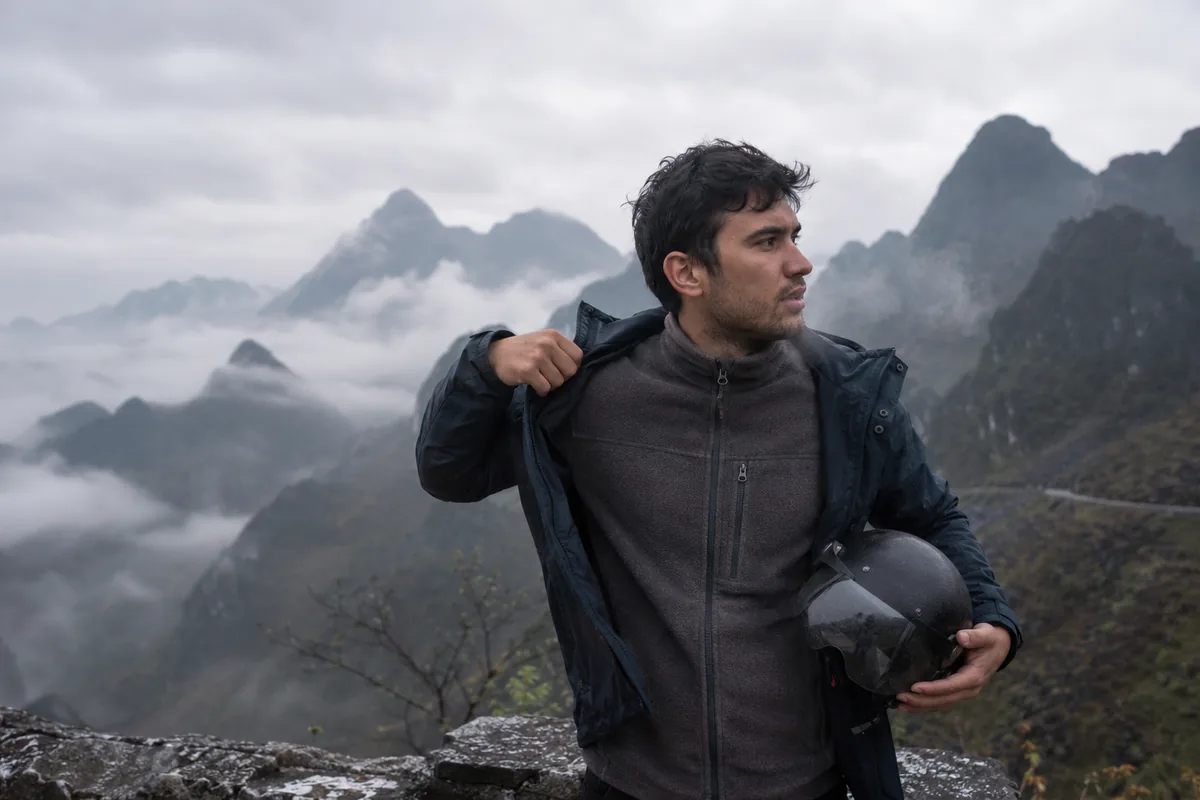 Traveller layering up against the cold mountain air at a misty Ha Giang Loop viewpoint.