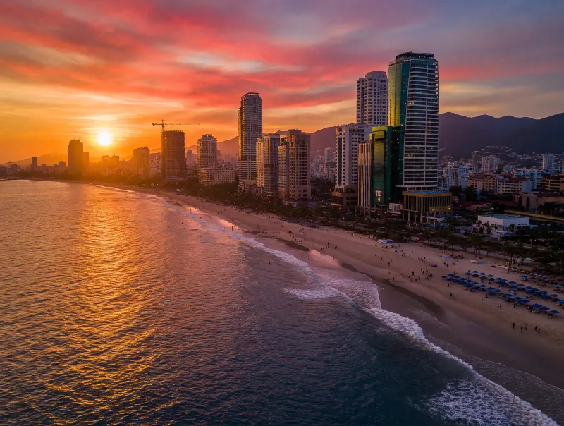 Da Nang skyline at sunset along My Khe Beach with high-rise buildings reflecting on the water