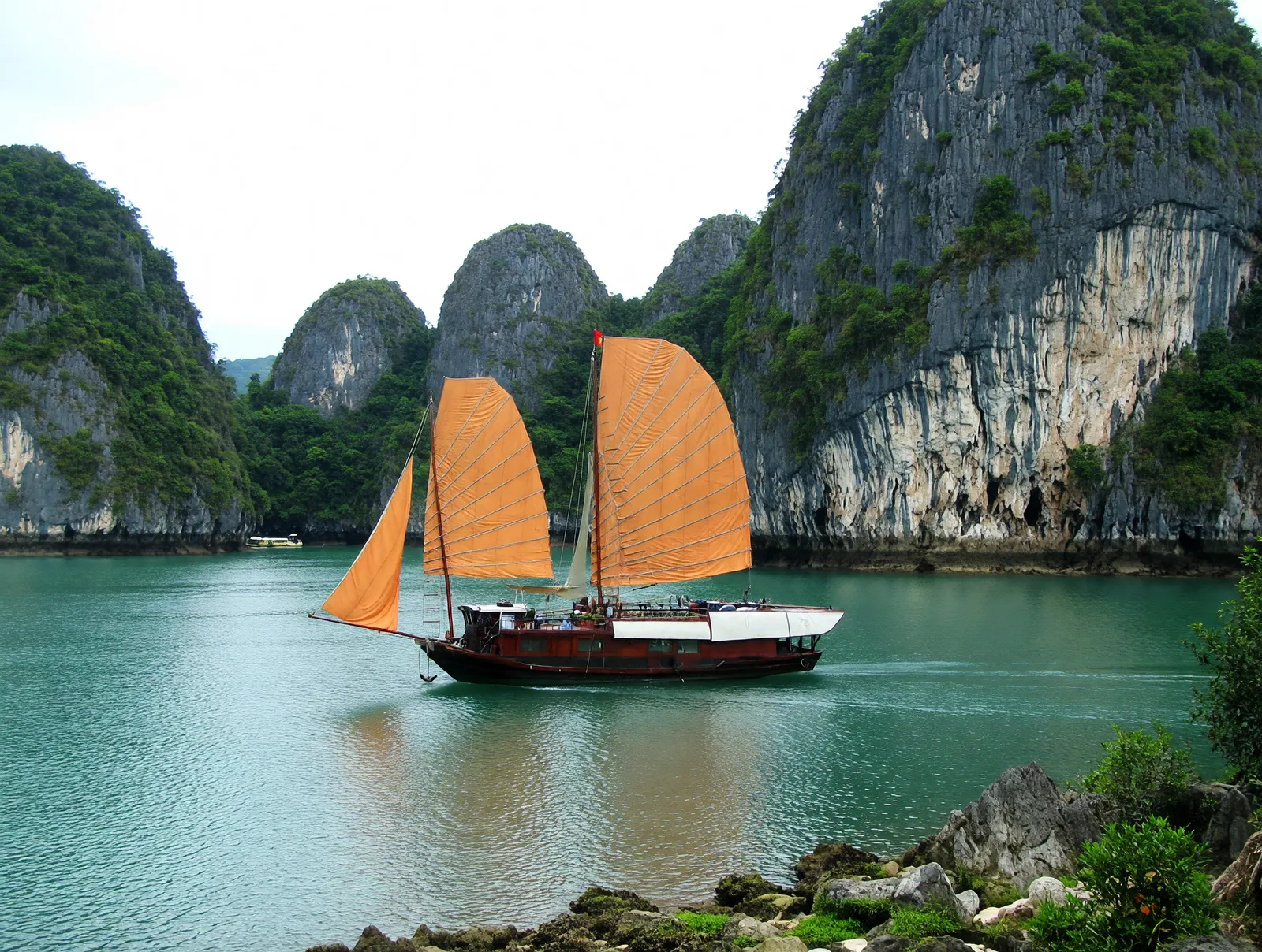 Traditional Vietnamese junk boat with orange sails cruising between limestone karsts in Ha Long Bay
