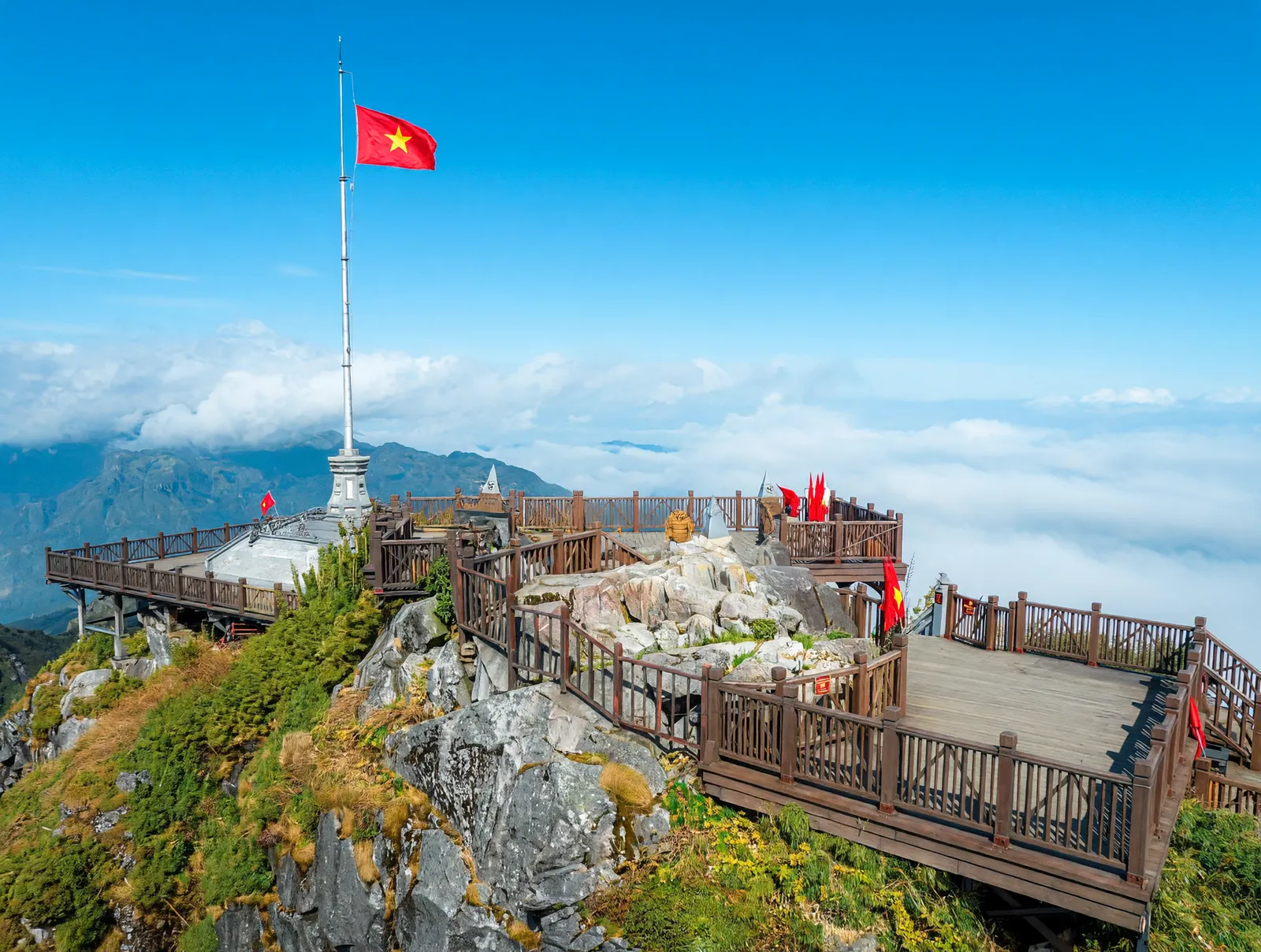 Vietnamese flag flying above the Fansipan summit viewing platform in Sapa, with clouds rolling beneath the boardwalk