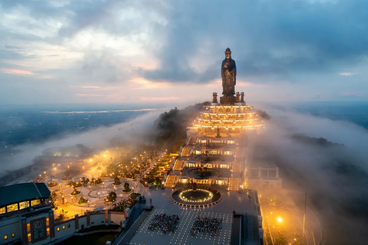 Tuong Phat Tay Bo Da Son bronze Buddha statue at Ba Den Mountain summit emerging through clouds at twilight