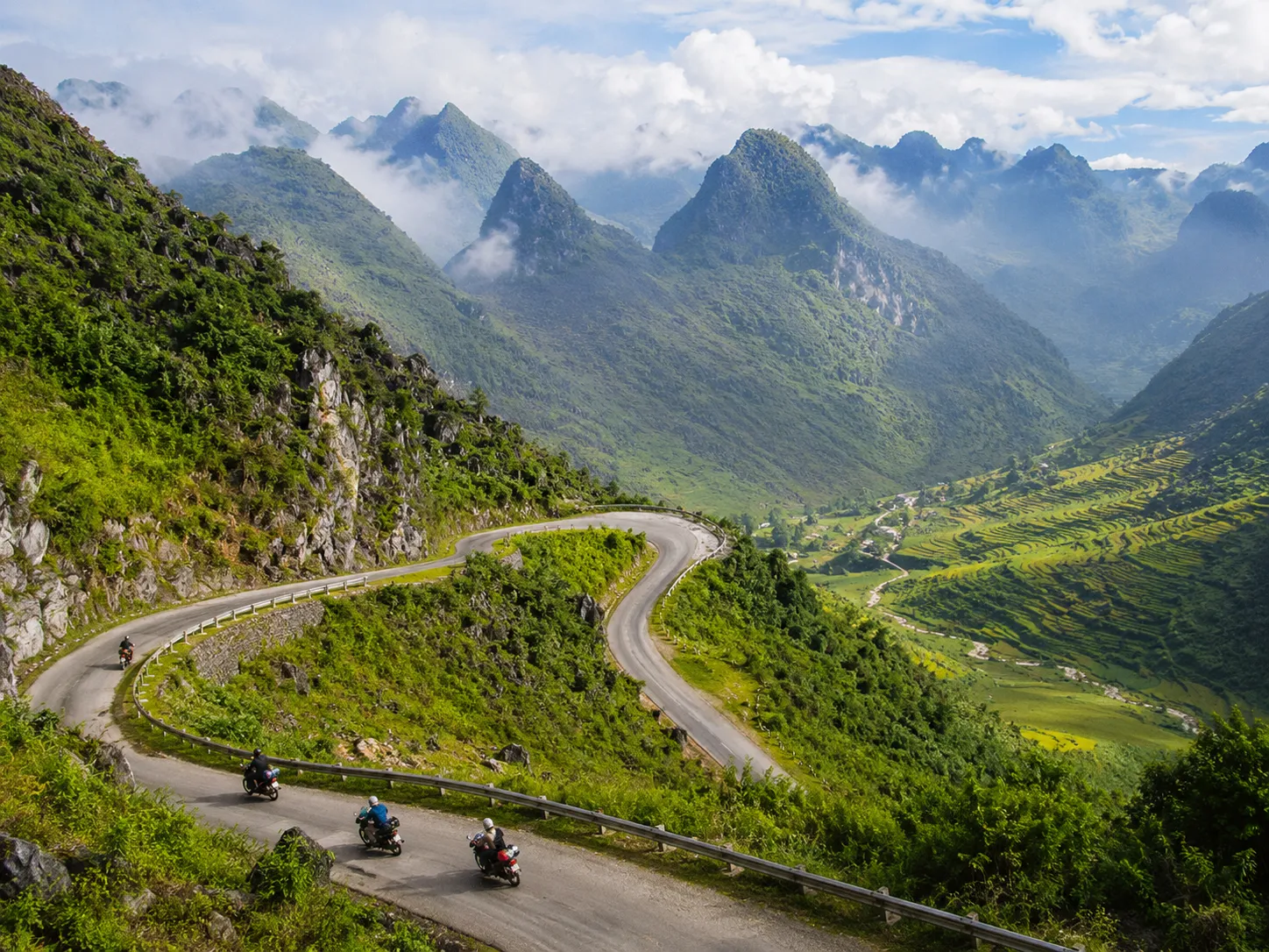 Winding mountain road through a green Ha Giang Loop valley with motorbike riders